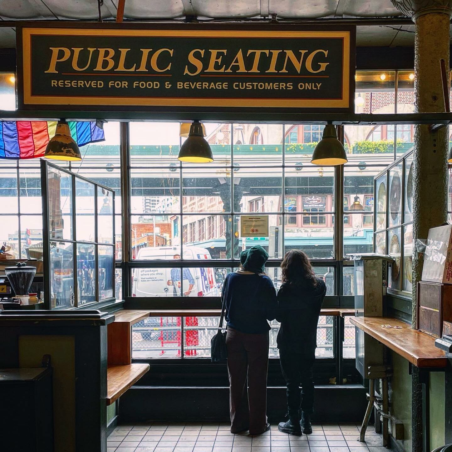 two people looking at Pike Place Market in Seattle through a window in a public seating area