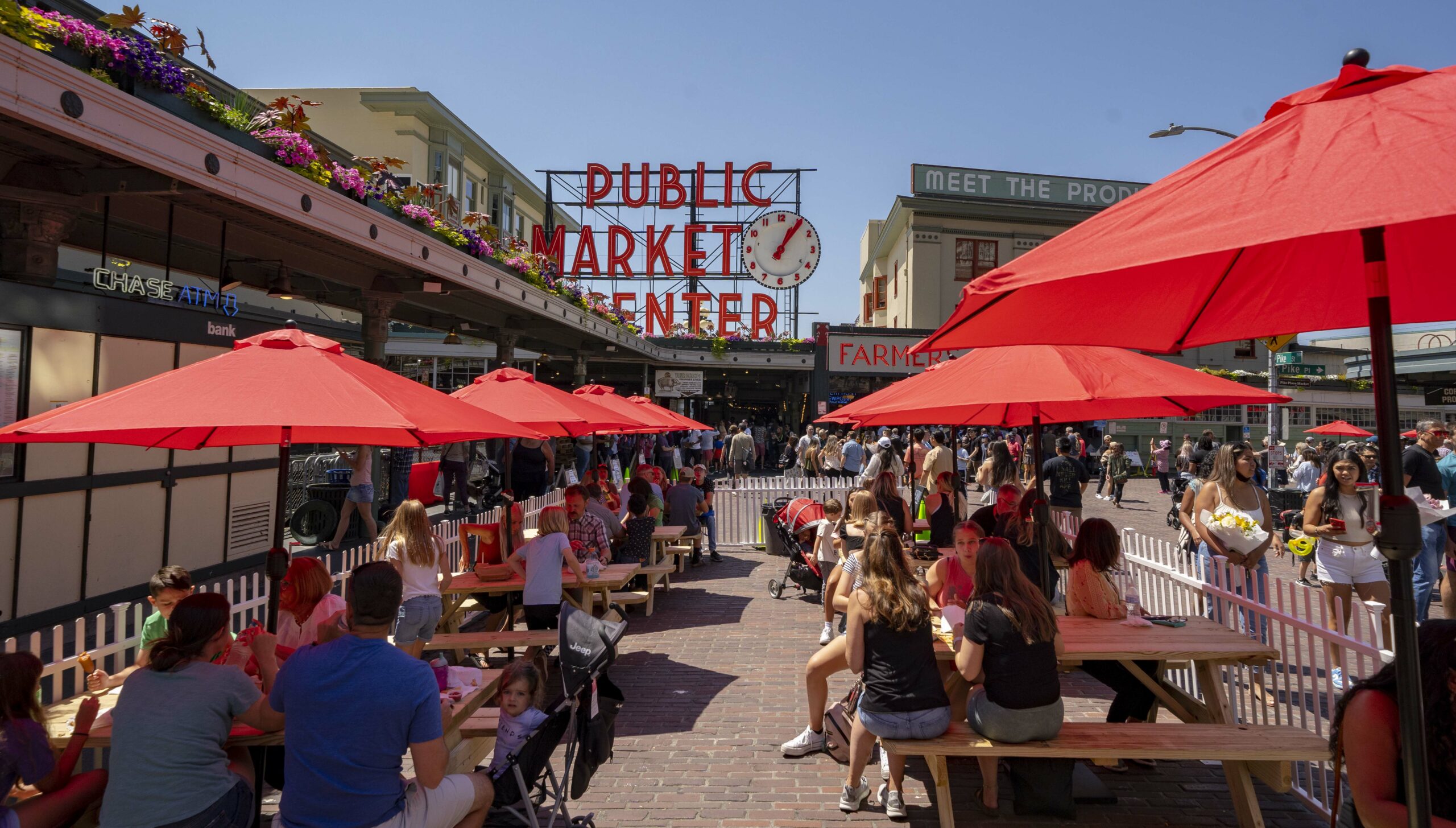 visitors siting at picnic tables in front of the famous Public Market Center Clock & Sign at Pike Place Market in Seattle