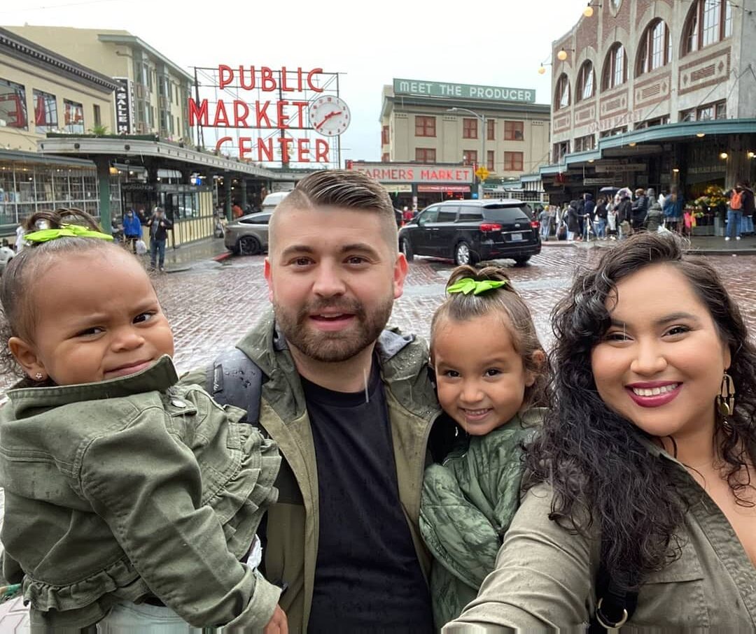 a family of four poses in front of the Public Market Center Clock and Sign at Pike Place Market in Seattle
